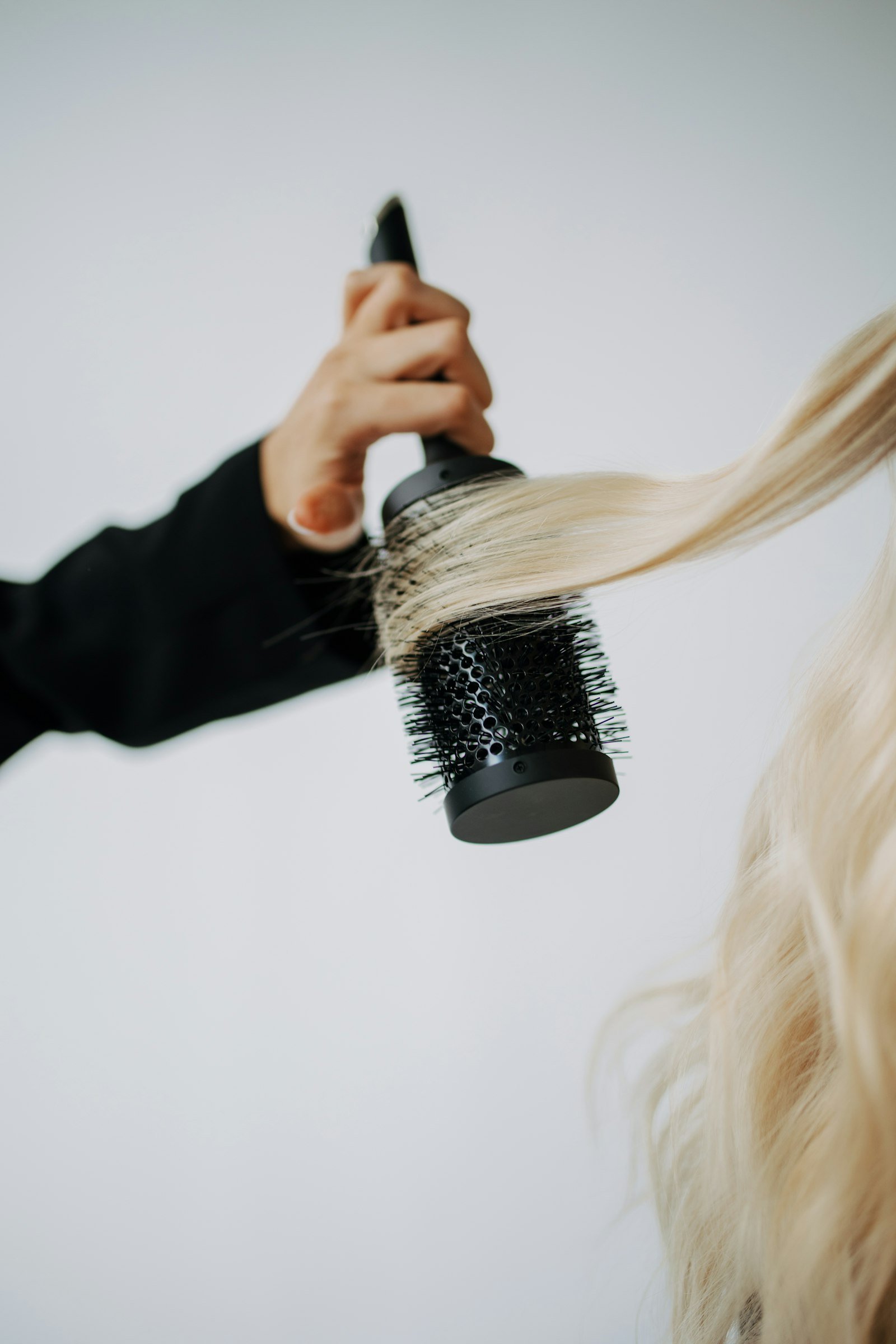 Mano cepillando cabello largo y rubio con cepillo redondo